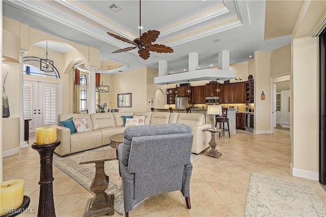 tiled living room with crown molding, ceiling fan with notable chandelier, and a raised ceiling