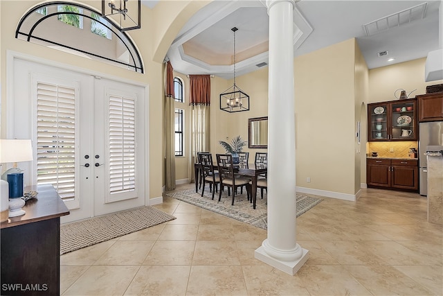 tiled entrance foyer featuring a towering ceiling, an inviting chandelier, french doors, and decorative columns