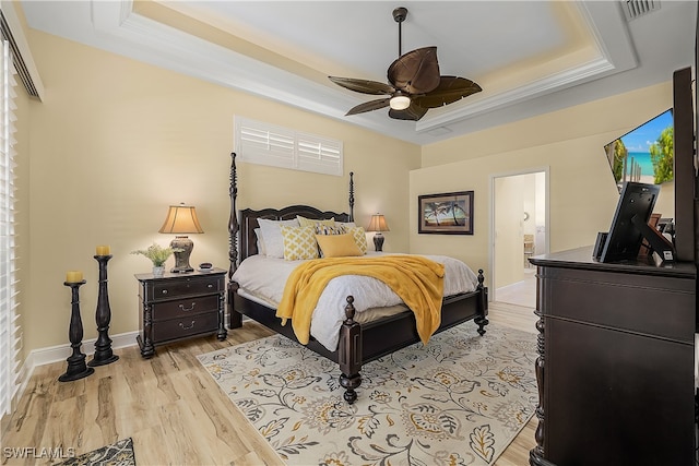 bedroom featuring a tray ceiling, ensuite bath, crown molding, light wood-type flooring, and ceiling fan