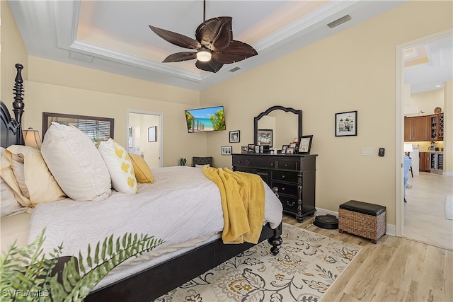 bedroom with ensuite bathroom, a raised ceiling, ceiling fan, light hardwood / wood-style floors, and ornamental molding