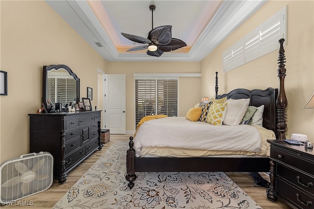 bedroom featuring light hardwood / wood-style flooring, ornamental molding, a raised ceiling, and ceiling fan