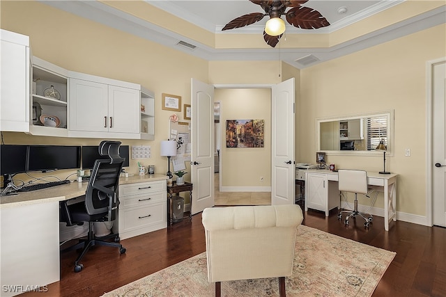 office area featuring built in desk, a tray ceiling, ceiling fan, dark wood-type flooring, and ornamental molding