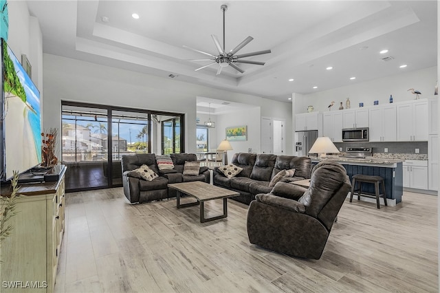 living room with ceiling fan, light wood-type flooring, and a raised ceiling