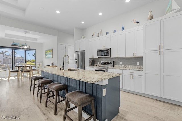 kitchen featuring white cabinets, an island with sink, light wood-type flooring, sink, and stainless steel appliances