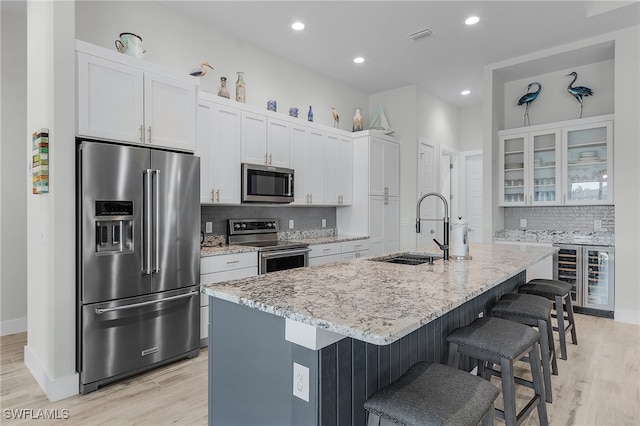 kitchen with beverage cooler, sink, stainless steel appliances, white cabinets, and a center island with sink