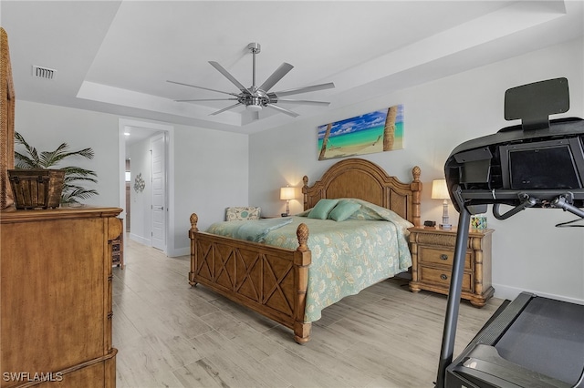 bedroom featuring a tray ceiling, light wood-type flooring, and ceiling fan