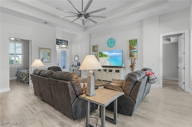 living room featuring light hardwood / wood-style flooring, a tray ceiling, and ceiling fan