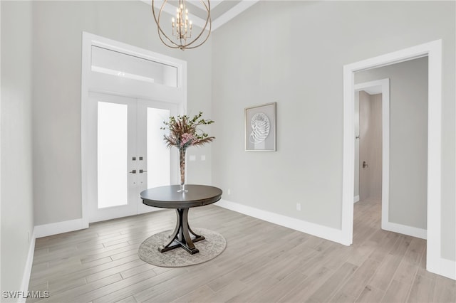 foyer entrance with a wealth of natural light, french doors, light hardwood / wood-style flooring, and an inviting chandelier