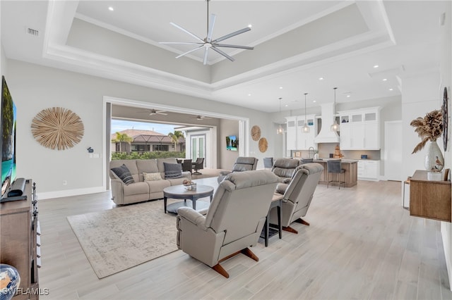 living room with light hardwood / wood-style flooring, a tray ceiling, and ceiling fan