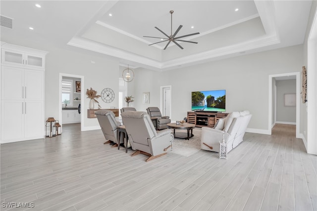 living room featuring a towering ceiling, a tray ceiling, light wood-type flooring, and ceiling fan