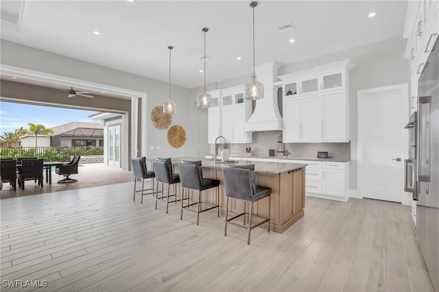 kitchen featuring a center island with sink, backsplash, white cabinets, and light hardwood / wood-style floors