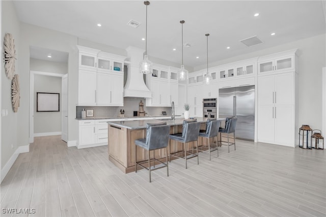 kitchen with a center island with sink, white cabinetry, stainless steel appliances, and light hardwood / wood-style floors