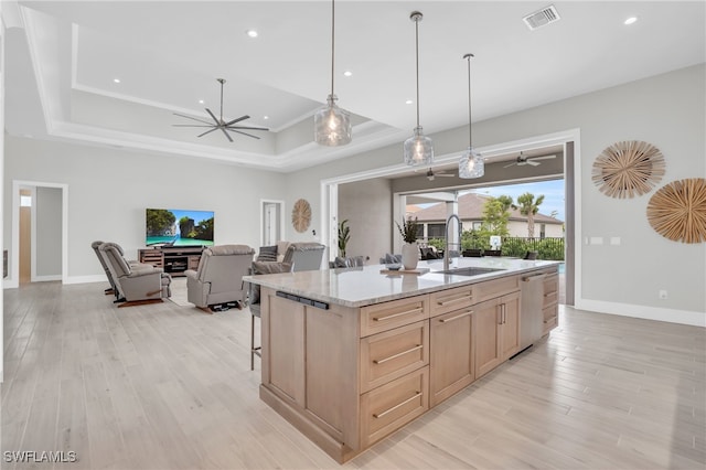 kitchen with light brown cabinets, a center island with sink, sink, light stone countertops, and light wood-type flooring