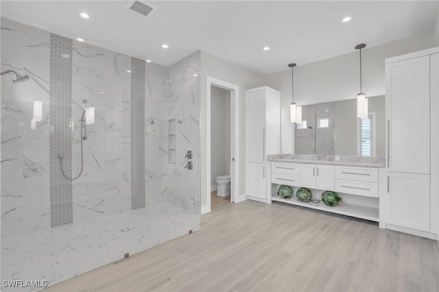 bathroom featuring vanity, toilet, a tile shower, and hardwood / wood-style floors