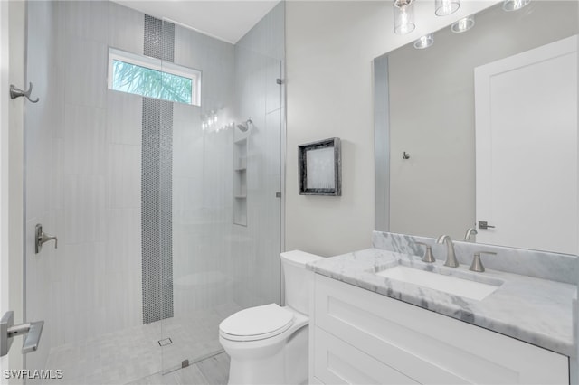 bathroom featuring vanity, a tile shower, and toilet