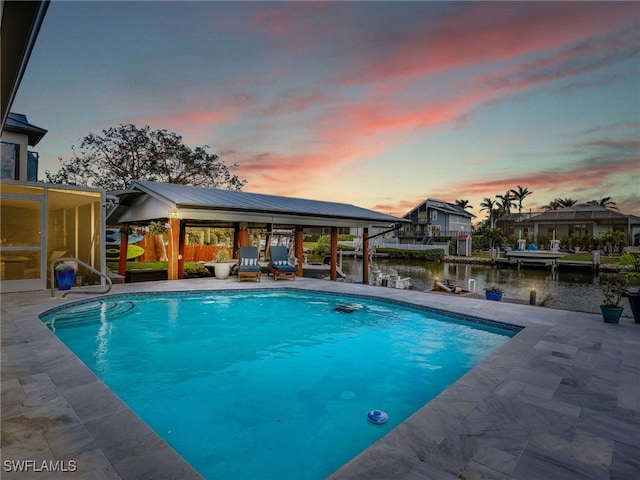 pool at dusk with a water view, a patio area, a gazebo, and a dock