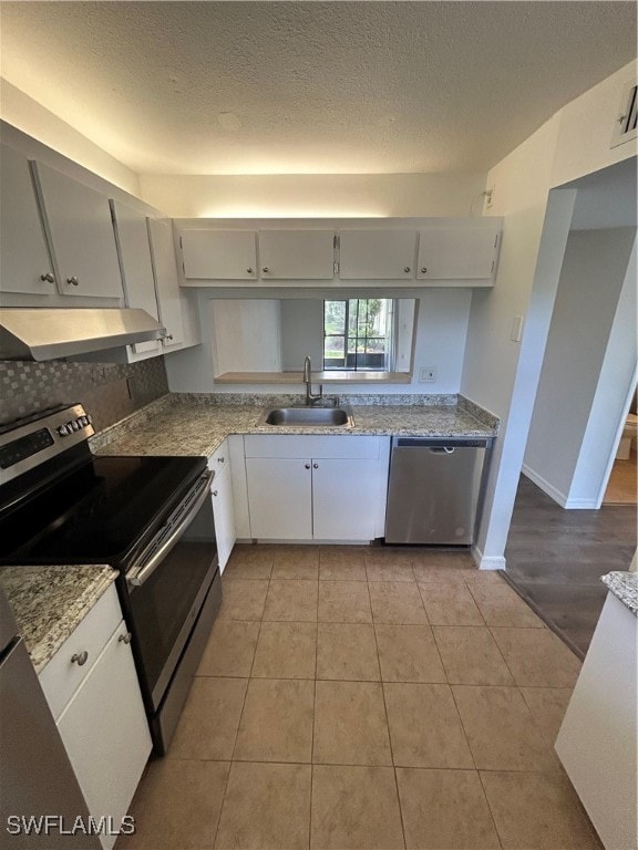 kitchen with sink, a textured ceiling, stainless steel appliances, light tile patterned floors, and exhaust hood