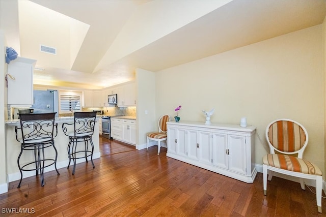 kitchen featuring a breakfast bar, kitchen peninsula, appliances with stainless steel finishes, white cabinetry, and wood-type flooring