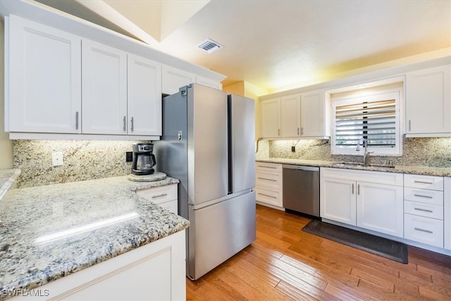 kitchen featuring light stone countertops, appliances with stainless steel finishes, sink, light hardwood / wood-style flooring, and white cabinetry