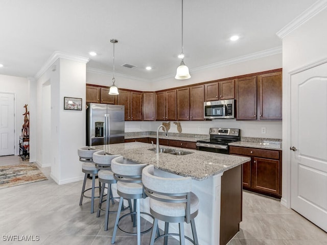 kitchen with appliances with stainless steel finishes, sink, an island with sink, pendant lighting, and light stone counters