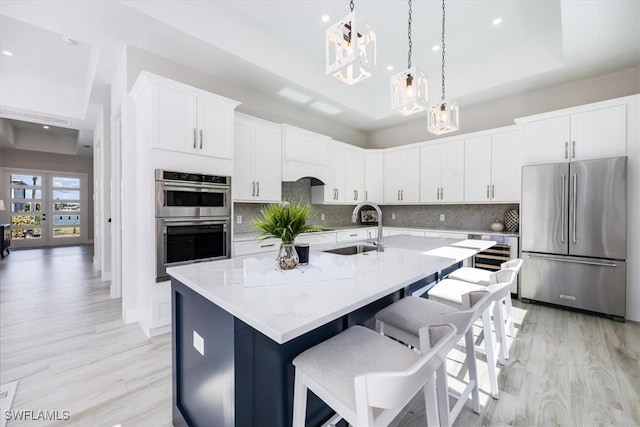 kitchen with appliances with stainless steel finishes, white cabinetry, sink, a raised ceiling, and a kitchen island with sink