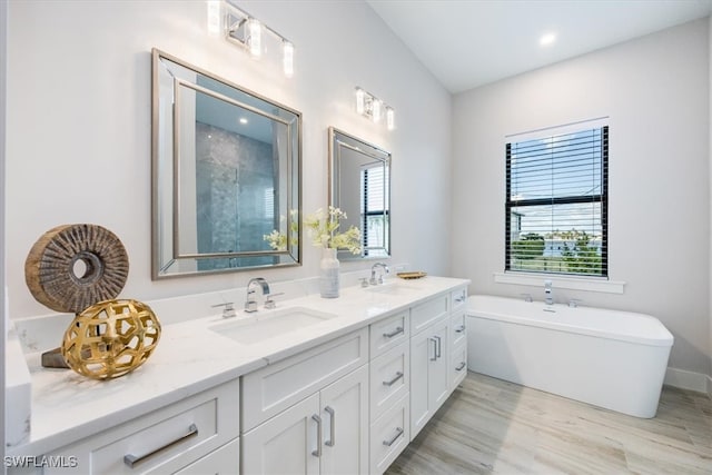 bathroom with double vanity, a soaking tub, a sink, and wood finished floors