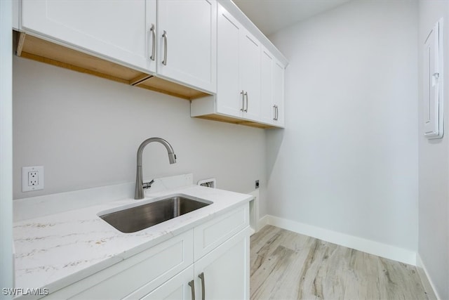 washroom with hookup for a washing machine, hookup for an electric dryer, a sink, light wood-style floors, and cabinet space