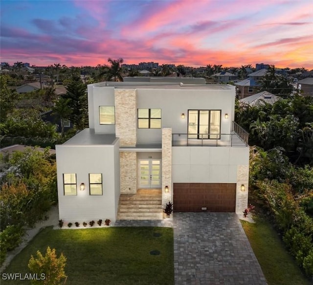 contemporary house with a balcony, stucco siding, decorative driveway, and french doors