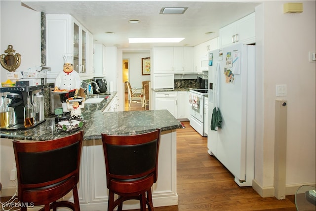 kitchen featuring hardwood / wood-style flooring, a breakfast bar area, kitchen peninsula, white cabinets, and white appliances