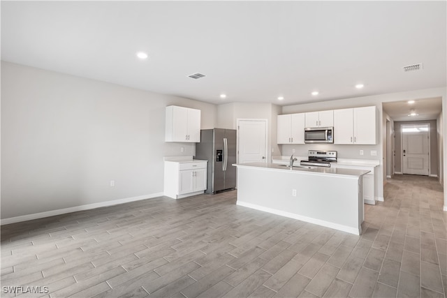 kitchen with sink, appliances with stainless steel finishes, a kitchen island with sink, white cabinets, and light wood-type flooring