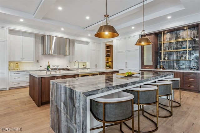 kitchen with a breakfast bar, pendant lighting, white cabinets, a large island, and wall chimney range hood