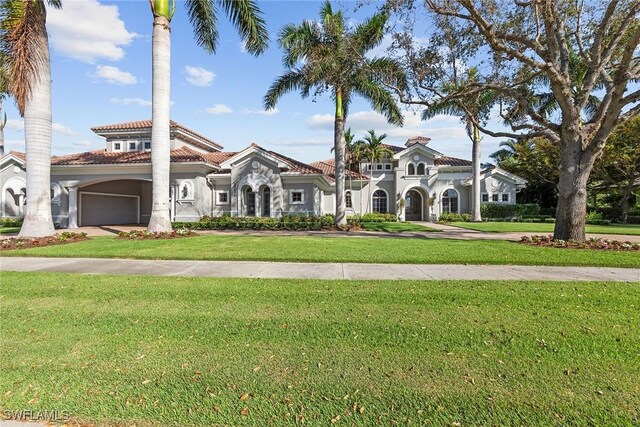 mediterranean / spanish home with a garage, a tile roof, a front lawn, and stucco siding