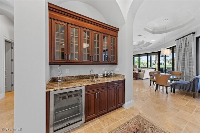 bar featuring indoor wet bar, stone tile flooring, a raised ceiling, a sink, and beverage cooler