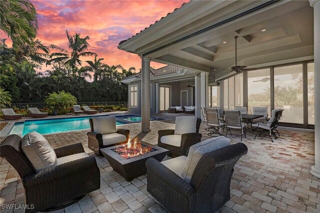 patio terrace at dusk with ceiling fan, an outdoor living space with a fire pit, and a fenced in pool