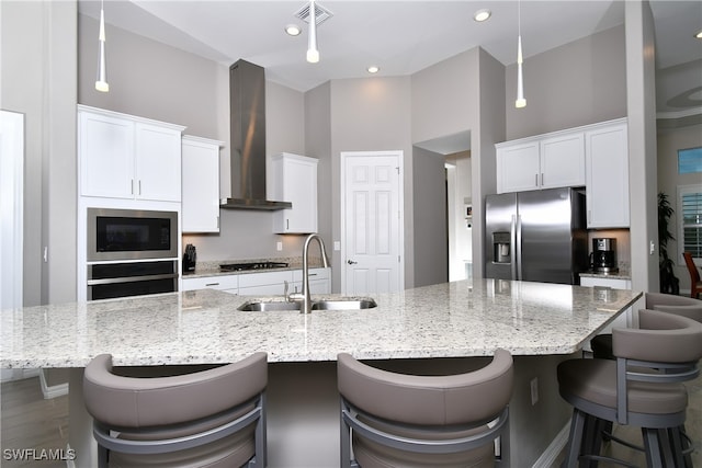 kitchen with stainless steel appliances, sink, wall chimney range hood, and a large island with sink