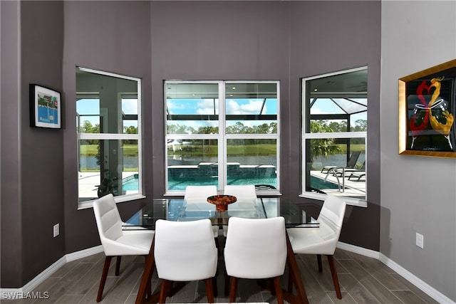 dining space featuring a towering ceiling, plenty of natural light, a water view, and wood-type flooring