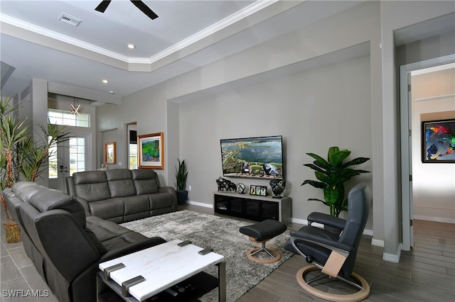 living room featuring wood-type flooring, ornamental molding, ceiling fan, and a tray ceiling