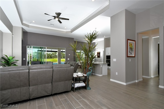 living room with ornamental molding, a raised ceiling, and ceiling fan