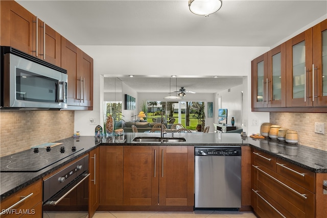 kitchen with sink, decorative backsplash, dark stone countertops, appliances with stainless steel finishes, and kitchen peninsula