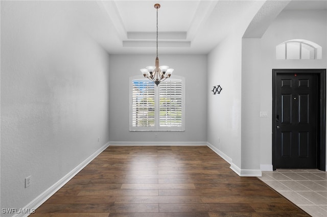 entryway with dark wood-type flooring, a tray ceiling, and a chandelier