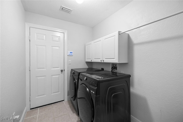 laundry room featuring washing machine and dryer, cabinets, a textured ceiling, and light tile patterned flooring