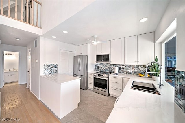 kitchen with stainless steel appliances, white cabinetry, ceiling fan, and light stone counters