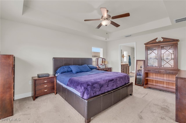 carpeted bedroom with ensuite bath, a tray ceiling, and ceiling fan