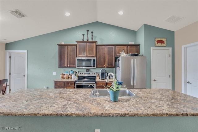 kitchen with appliances with stainless steel finishes, sink, dark brown cabinets, vaulted ceiling, and a center island with sink