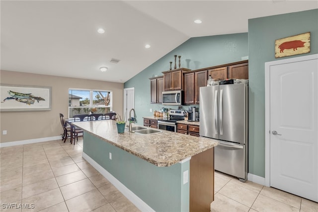 kitchen with appliances with stainless steel finishes, sink, lofted ceiling, light tile patterned floors, and a center island with sink