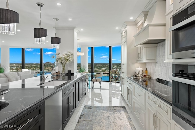 kitchen featuring premium range hood, sink, decorative light fixtures, expansive windows, and white cabinets