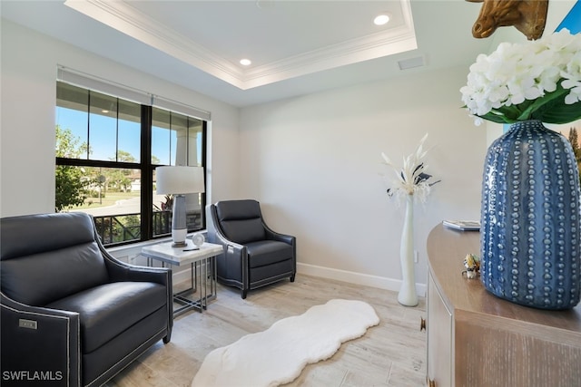 sitting room with light hardwood / wood-style floors, crown molding, and a tray ceiling