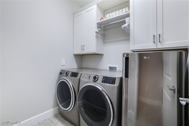 laundry room with washing machine and clothes dryer, cabinets, and light hardwood / wood-style flooring