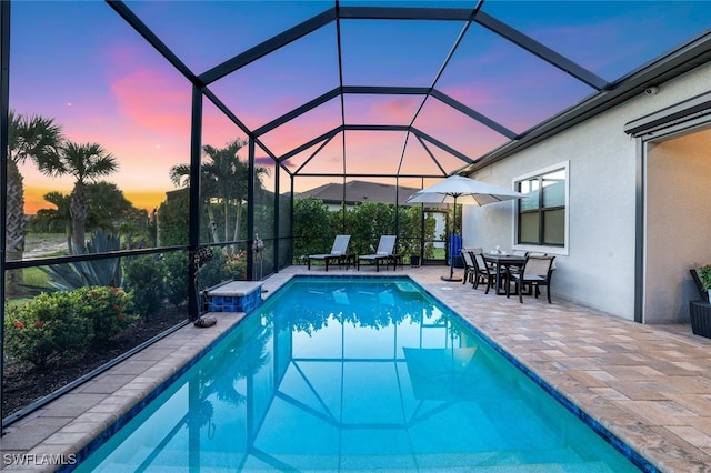 pool at dusk featuring a lanai and a patio