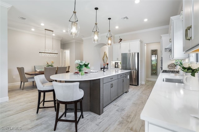 kitchen featuring stainless steel refrigerator, a large island with sink, decorative light fixtures, white cabinets, and light wood-type flooring